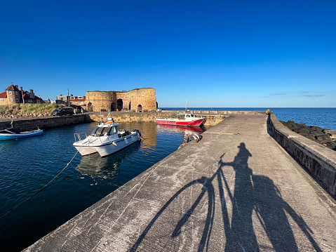 A shadow of an unrecognisable person who has been bike riding, stopping at the harbour in Beadnell, North East England. All that can be seen is the harbour and the shadow of the person and their bike.