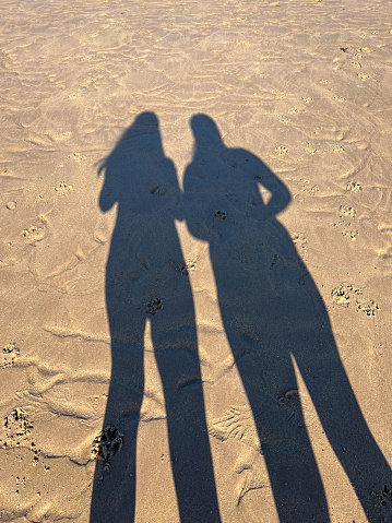 A shadow of two unrecognisable people on the beach in North East England. They are standing side by side in the sun.