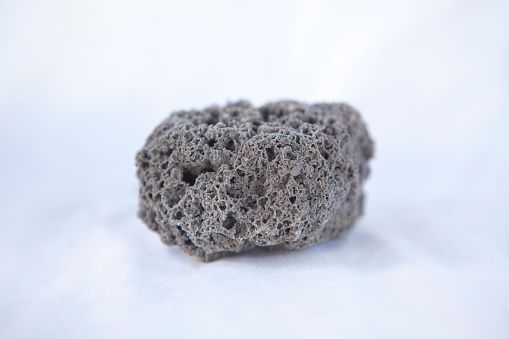 Unpolished black pumice rock cutout. Isolated over white fabric cloth
