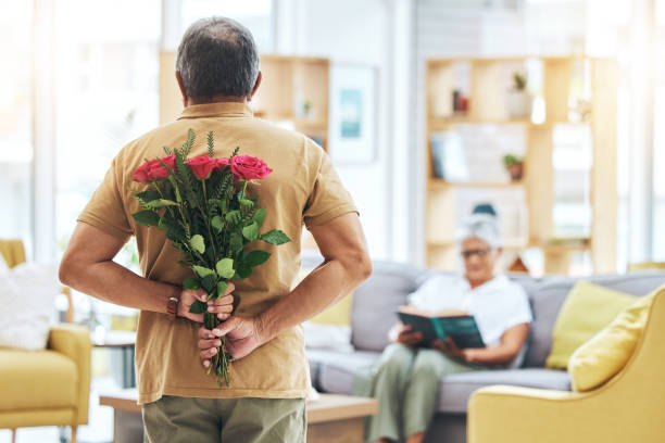 istock Love, surprise and senior man with roses behind back for romance, gratitude and commitment to wife in living room of home. Couple, person and flowers in hand for gift and marriage anniversary 1693694456
