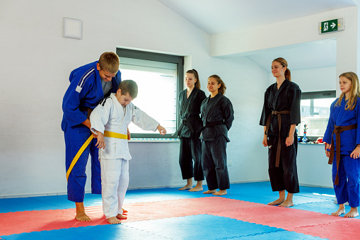 A teenager ties a yellow belt to a martial arts student.