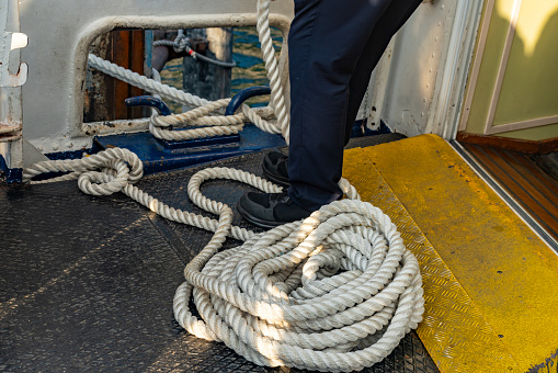 Stainless steel boat mooring cleat with knotted rope mounted on white yacht deck