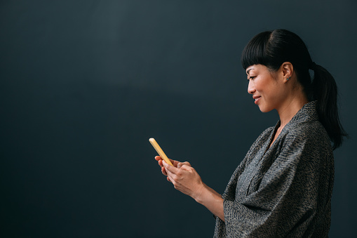 Smiling Asian woman texting on her mobile phone (copy space).