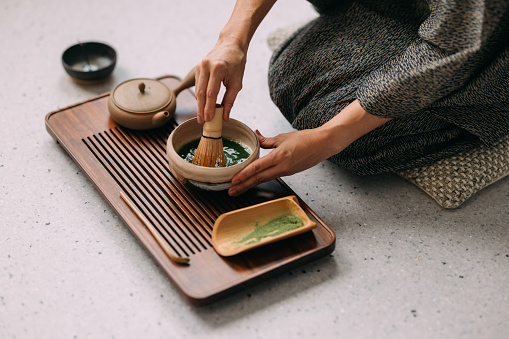 Participating in a tea ceremony, a Japanese woman in kimono carefully brews tea.