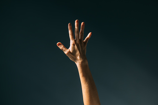 Reaching out: a woman's hand in sunlight, gray background.