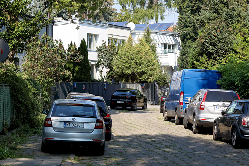 Warsaw, Poland - September 13, 2023: There is a narrow street next to the houses and there are cars parked on both sides of the street in Saska Kepa housing estate, part of the Praga-Poludnie district