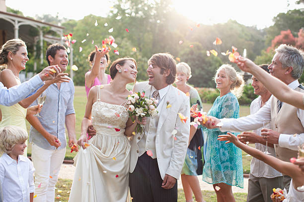 guests throwing rose petals on bride and groom - bloemblaadje fotos stockfoto's en -beelden