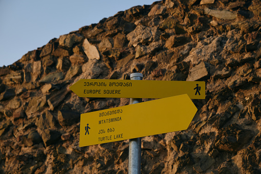 Yellow tourist sign for a walking route in the center of Tbilisi, old town. Arrow to Europe Square in one direction, arrow to Mtatsminda Park and turtle Lake in the other direction