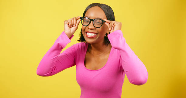 istock Beautiful Black woman pulls silly face trying eyeglasses, yellow studio 1693792519