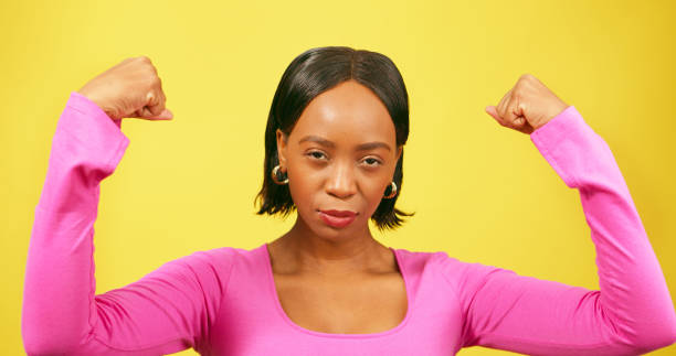istock Beautiful strong woman flexes both arms, muscle, yellow studio background 1693793134