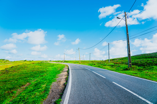 Concrete road with electric poles surrounded by green fields
