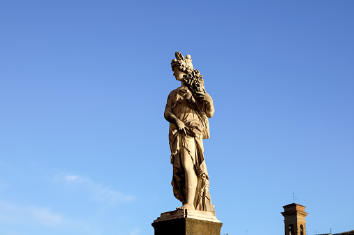 Florence, Italy - April 16, 2023: One of the statues of the four seasons. The historic statue of Summer by Giovanni Caccini, part of the Ponte Santa Trinita, can be seen against the blue sky.