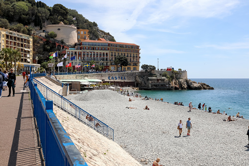 Nice, France - April 28, 2023: The promenade along the Mediterranean Sea and the beach are frequented by tourists and locals. Nearby buildings are visible.