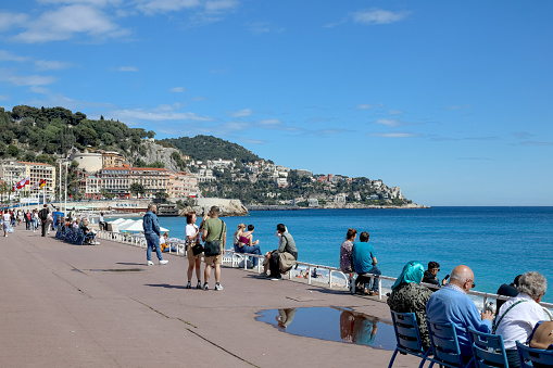 Nice, France - May 2, 2023: The promenade along the shore of the Mediterranean Sea is frequented by tourists and locals. The nearby peninsula and buildings are visible.