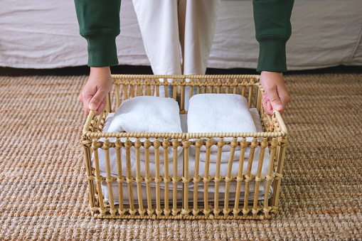 Closeup image of a woman holding a wooden basket of towels at home