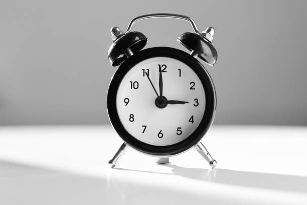 白とグレイの背景にレトロなスタイルのモダンな白黒目覚まし時計と、午後の3時間の時間を示す影。シエスタの時間、休憩、昼食のコンセプト。