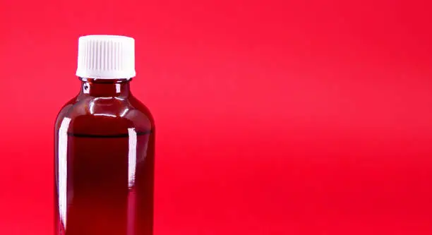 Photo of empty glass medicine bottle on red background