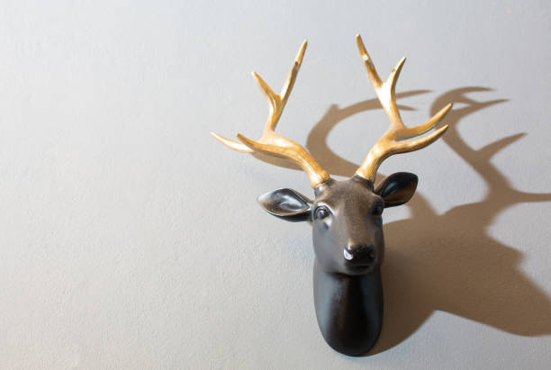 una scultura di testa di cervo nero con corna dorate è montata su un muro di cemento bianco. - deer stag wall animal head foto e immagini stock