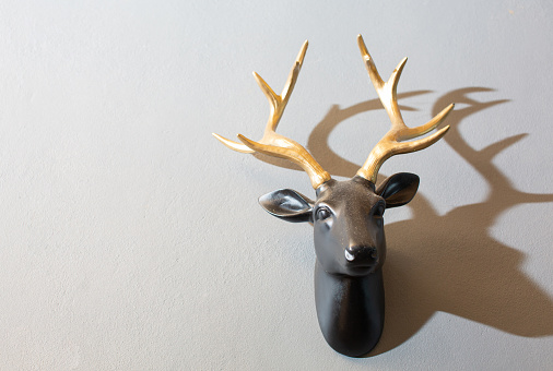 A black deer head sculpture with golden horns is mounted on a white cement wall.