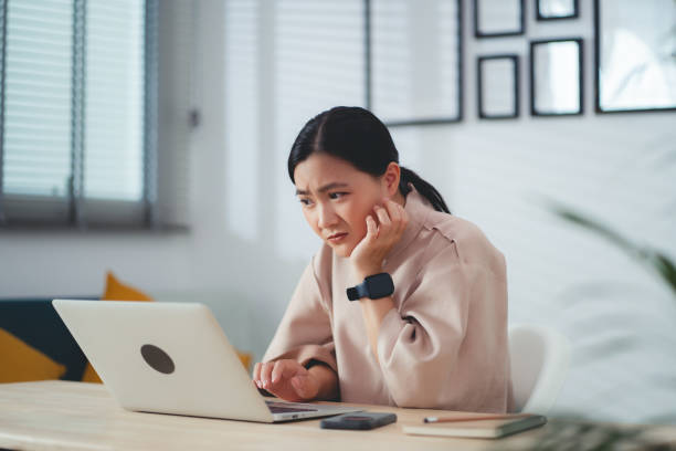Asian woman using laptop, thinking about project and feel confused.