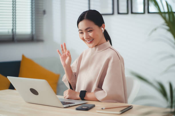 istock Asian woman wearing earbud showing OK sign using laptop talking on video conference sitting at home office. 1693877310