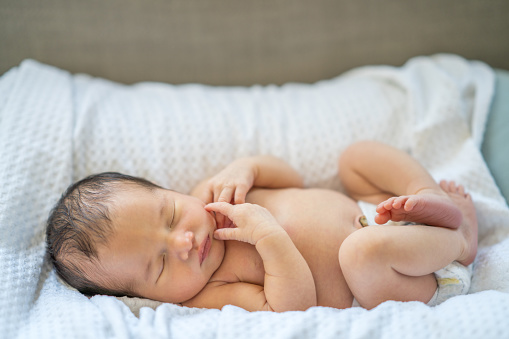 Sleeping newborn baby in a wrap on white blanket. Beautiful portrait of little child girl 7 days, one week old. Baby smiling in a dream.