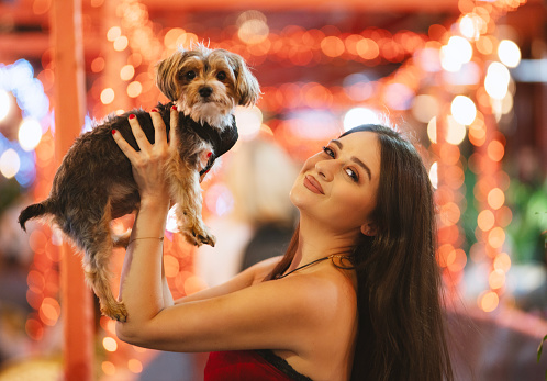 Young beautiful woman with her terrier puppy standing on city street with neon lights late in the evening, New York City