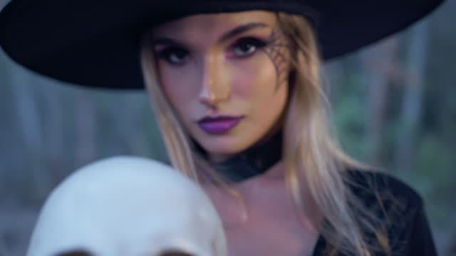 A mysterious witch, deep in the forest, holds a skull and gazes directly at the camera, exuding an aura of enchantment and mystique,halloween theme.