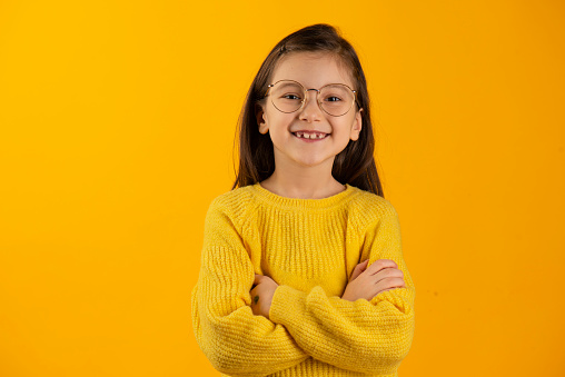 Girl in a yellow sweater looks at the camera on a yellow background.