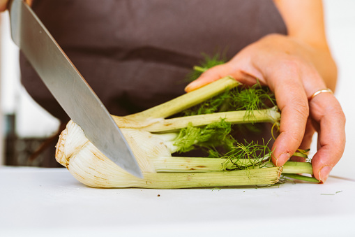 An unrecognizable woman uses a sharp knife to cut vegetables on a wooden cutting board.