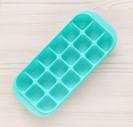 Closeup of a generic, plastic ice cube tray on a whitewashed wood background.