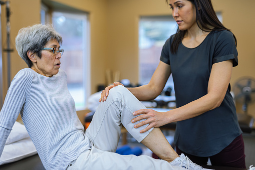 Selective focus on the hands of a physical therapist as she holds the knee of a senior female patient as they work on improving leg strength and mobility.