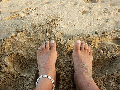 Feet of a man on the beach sand adorned with an ankle bracelet