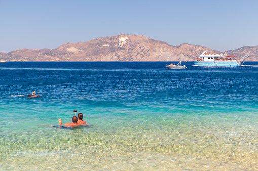 Zakynthos, Greece - August 16, 2016: Tourists take photos with selfie stick in water on the beach on a sunny summer day