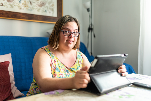 Portrait of a cheerful girl with special needs using a digital tablet sitting on the sofa at home