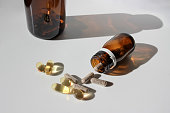 pills of dietary supplements and fish fat oil Omega-3 capsules spilling out of brown bottle on white background with hard sun shadow