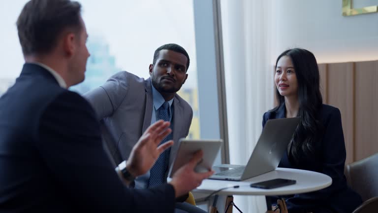 Caucasian businessman is holding tablet to show and explain business plan to multiracial business people in the office lobby.