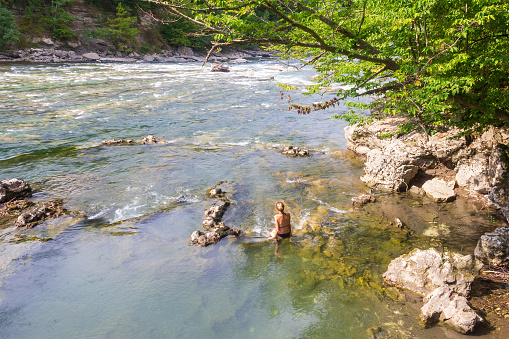 a young woman, a girl is sitting in the water of a mountain river on a hot summer day