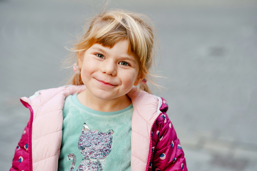 Portrait of happy smiling toddler girl outdoors. Little preschool child with blond hairs looking and smiling at the camera. Happy healthy child enjoy outdoor activity and playing