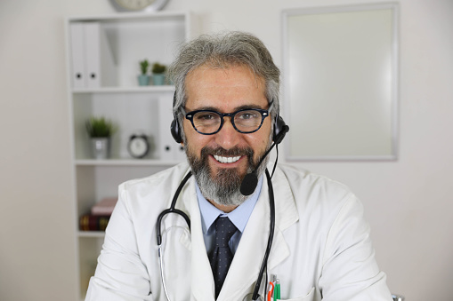 Portrait of a senior smiling doctor, sitting at a desk and looking at the camera. The medical director of the hospital wears a uniform and exudes confidence