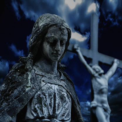 Ancient statue of the Virgin Mary on the background of the crucifixion of Jesus Christ. Conceptual Bible photography: death, resurrection and victory over the death of Jesus Christ.