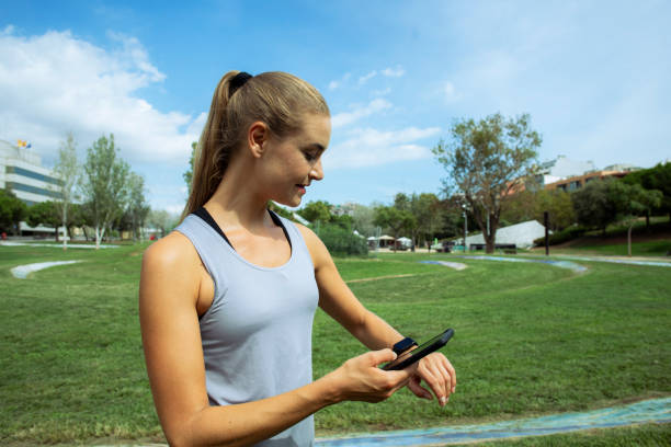 Young woman exercising in the park Checking the smart cell phone tecnología inalámbrica stock pictures, royalty-free photos & images