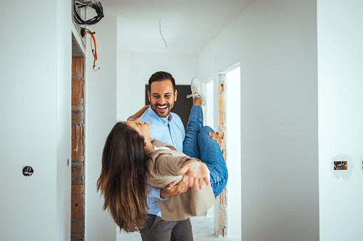 Happy Couple Dancing Together Out Of Happiness For Buying New Apartment. Young cheerful couple having fun while dancing during their home renovation process.