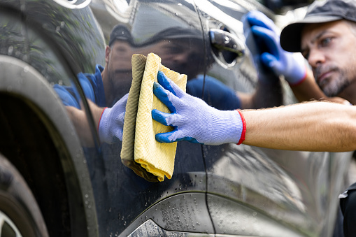 Man holds microfiber cloth and polishing car outdoors