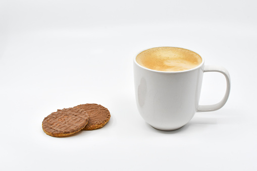 Mug of hot frothy coffee and chocolate biscuits isolated on a plain white background. Copy space.
