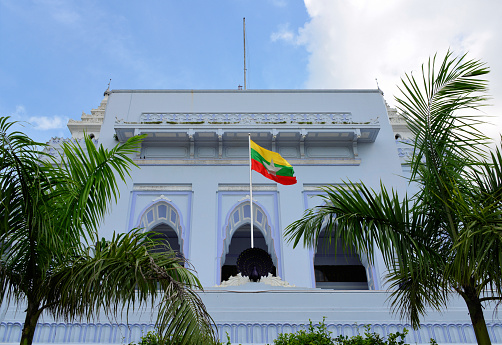 Yangon / Rangoon, Myanmar / Burma: Myanmar flag on the balcony of Yangon City Hall is the seat of the city's administrative body, Yangon City Development Committee (YCDC). The building is considered a fine example of syncretic Burmese architecture, featuring traditional tiered roofs called pyatthat, and was designed by Burmese architect U. It used to be called the Yangon Municipal Corporation Building. Since 1934, the presidents of corporations have been called mayors.