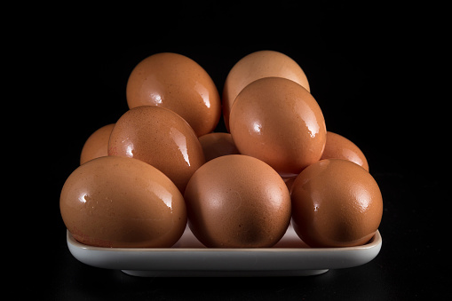 still life with eggs, contrast in dark colors, wet eggs on light tray and deep dark background