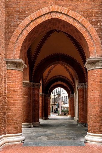 Passage through red brick walls and columns under vaulted ceiling in old town of Alba, Italy (vertical composition).