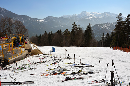 Many skis and ski poles of vacationing tourists are laid on the slope of a snowy mountain for downhill skiing near a resting place