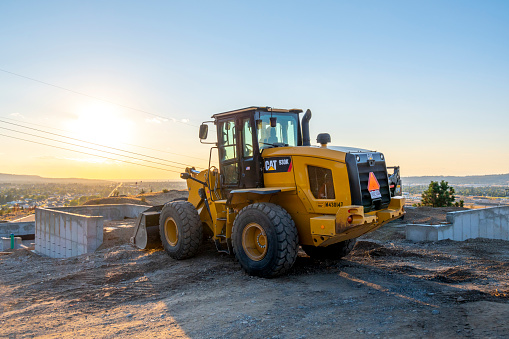 A tractor ready to move dirt and excavate on a hilltop new construction site overlooking the city of Spokane, Washington, USA near sunset.